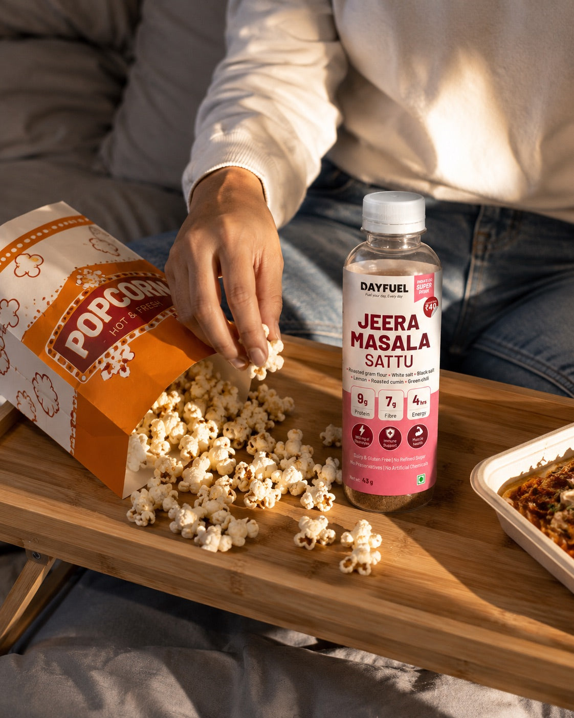 A bottle of Dayfuel Jeera Masala Sattu on a bed tray next to a spilled packet of popcorn